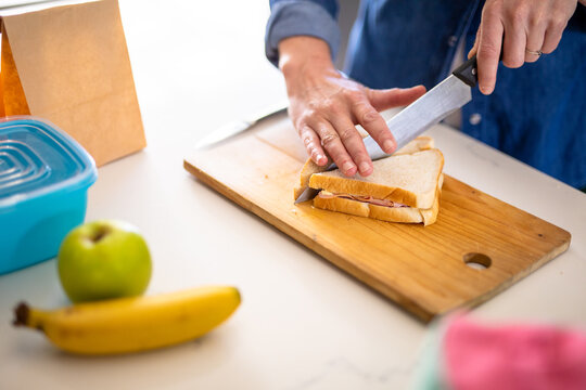 Midsection of caucasian mature woman cutting sandwich for lunch box