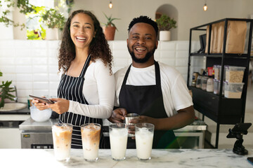 Portrait of cheerful african american baristas with iced coffee glasses on counter in cafe