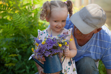 Happy grandfather with his granddaughter picking a flowers in the garden