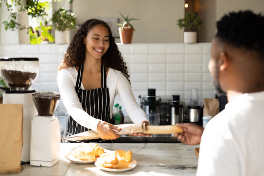 Smiling african american barista serving male customer at counter in coffee shop