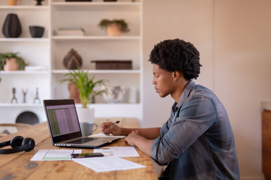 Side view of african american young businessman writing while using laptop at table