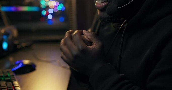 A dark room lit by led lights, a man with black leather sits in front of a computer at night talking through a headset to team members rubbing hands together before the next round.