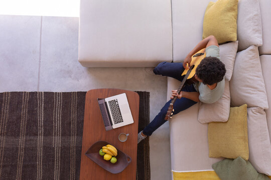 Directly above shot of african american young man playing guitar while with laptop at home