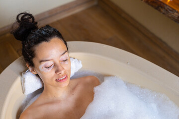 High angle view of biracial young woman with eyes closed relaxing in soapy bathtub at spa