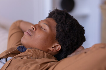 Close-up of african american young man with eyes closed and hands behind head relaxing at home