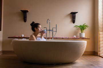 Biracial young woman drinking coffee in bathtub by wall at spa, copy space