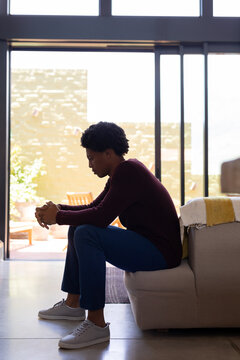 Side view of thoughtful african american young man with hands clasped sitting on sofa at home