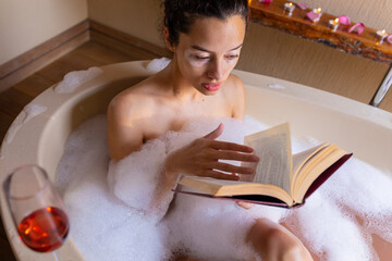 High angle view of biracial young woman reading book in bathtub at spa