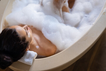 High angle view of biracial young woman relaxing in soapy bathtub in spa