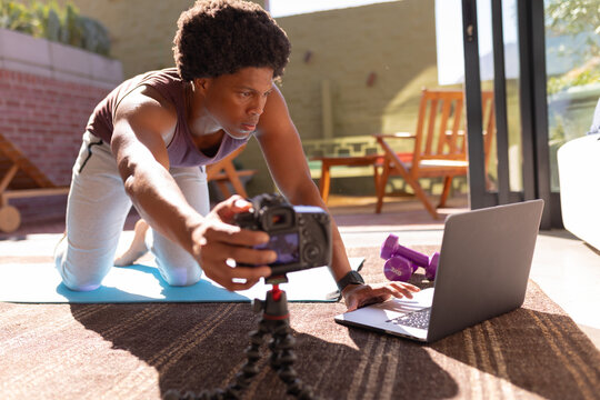 African american young man adjusting camera while using laptop for making vlog on exercise at home