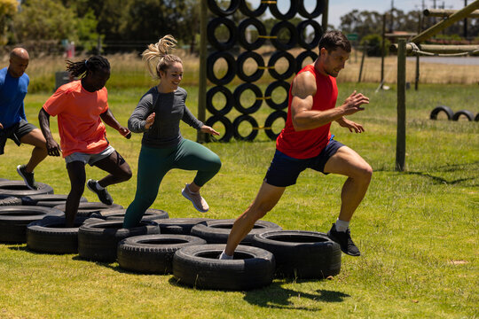 Group Of Male And Female Fit People Running On Tires During Obstacle Course At Boot Camp