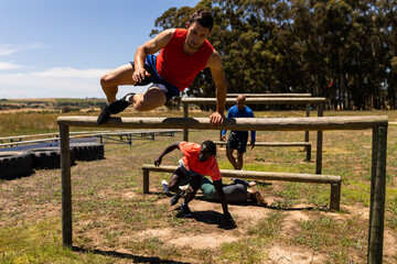 Group of male and female fit people jumping over wooden hurdles during obstacle course at boot camp