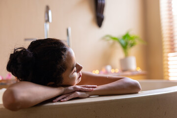 Thoughtful biracial young woman leaning on bathtub in spa
