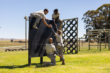 Two diverse male soldiers helping female caucasian soldier to climb wooden wall at boot camp