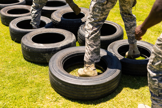 Low section of diverse male and female soldiers walking on tires during obstacle course at boot camp