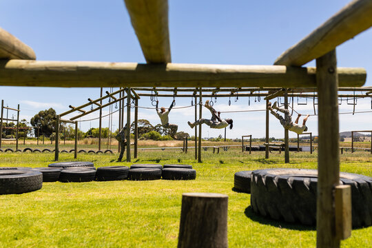 Group of male and female diverse soldiers rope climbing during obstacle course at boot camp