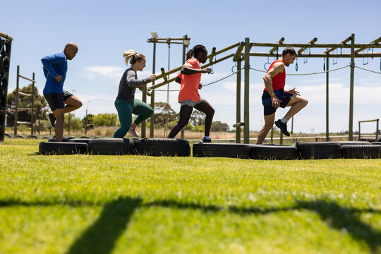 Group of male and female fit people running on tires during obstacle course at boot camp