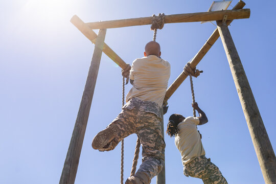 Two african american male soldiers rope climbing during obstacle course at boot camp