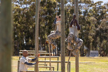 Two diverse male and female soldiers rope climbing during obstacle course at boot camp