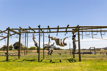 Group of male and female diverse soldiers rope climbing during obstacle course at boot camp