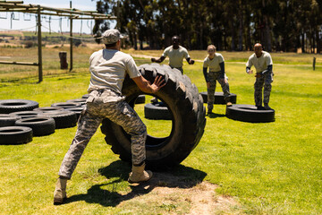 Rear view of a male soldier flipping a tire during obstacle course at boot camp