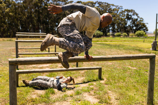 African american male soldier jumping over wooden hurdles during obstacle course at boot camp