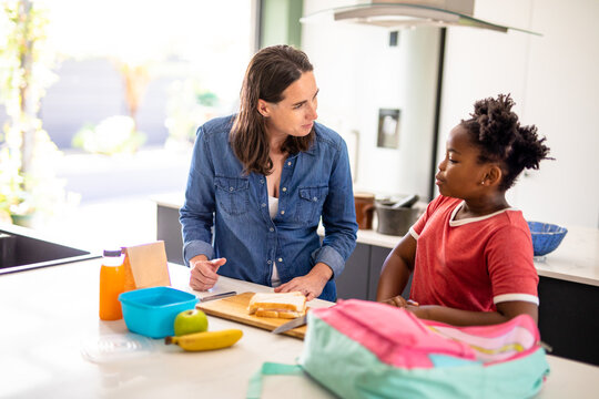 Caucasian mature woman talking to african american daughter while packing lunch box in kitchen