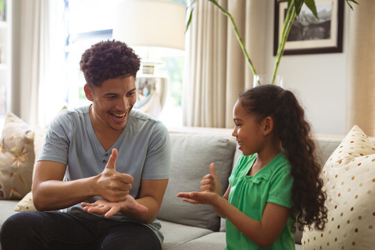 Happy biracial father and daughter communicating through sign language at home