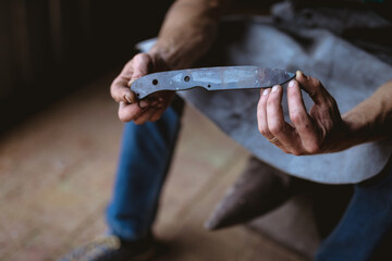 Low section of blacksmith holding knife shaped metal while sitting in industry