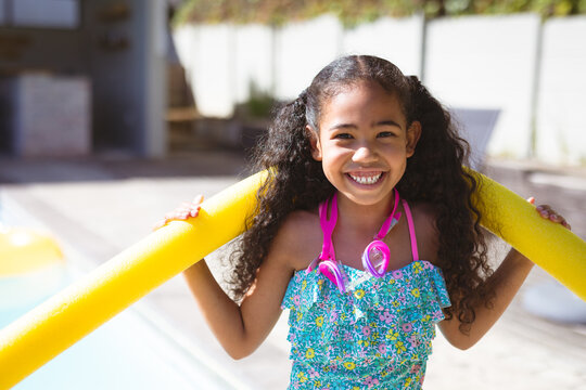 Portrait of smiling biracial girl holding yellow swimming float around neck at backyard on sunny day
