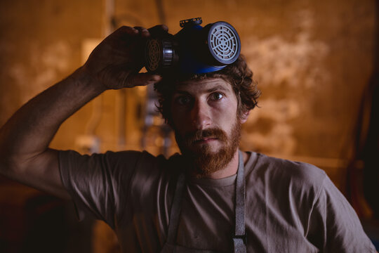 Portrait of bearded caucasian blacksmith with gas mask in manufacturing industry