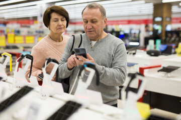 Fototapeta na wymiar European man who came to an electronics store with his wife chooses a mobile phone to buy it