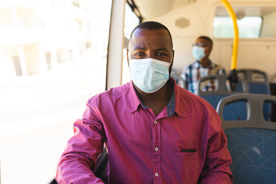 African american businessman wearing a face mask sitting on the bus while on the go to office
