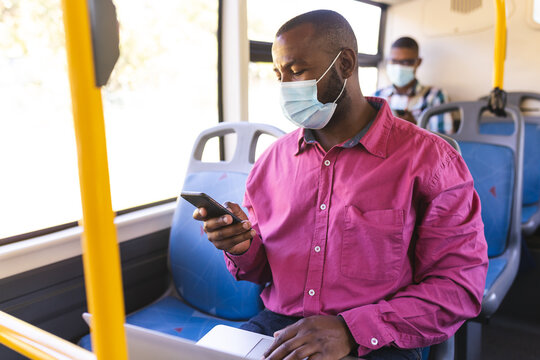 Businessman wearing a face mask with laptop using smartphone on the bus while on the go to office