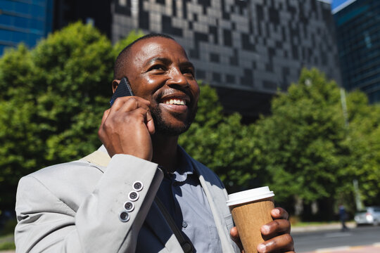 African american businessman with coffee cup talking on smartphone on the street on the go to office