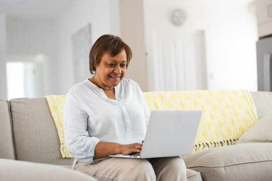 Smiling african american senior woman using laptop while sitting on sofa at home