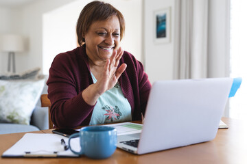 Happy senior african american woman waving hand on laptop during online doctor consultation at home