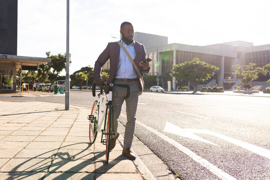 African american businessman with bicycle using smartphone on the street on the go to office