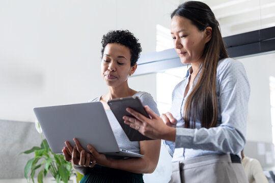 Multiracial creative businesswomen with laptop and digital tablet discussing in office