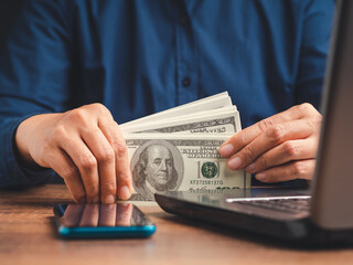 A businessman in a blue shirt holds US banknotes while sitting at the table in the office