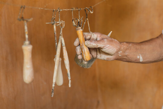 Cropped image of male potter hanging messy pottery tools on string by wooden wall in workshop