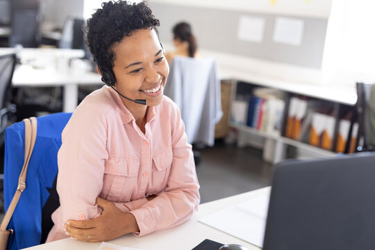 Biracial female customer representative smiling while talking through headset in office