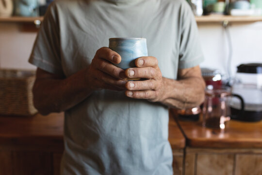 Midsection of caucasian mature man holding coffee mug in kitchen at cob house