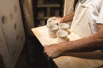 Midsection of male potter carrying earthenware on wooden plank in workshop