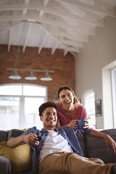 Happy young biracial couple watching tv enjoying together in living room at home