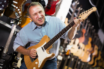 happy man is playing on electric guitar and satisfied it in music store.