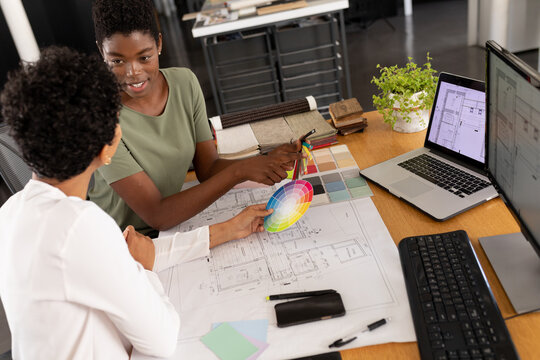 Multiracial female architects discussing over color swatch at desk in creative office