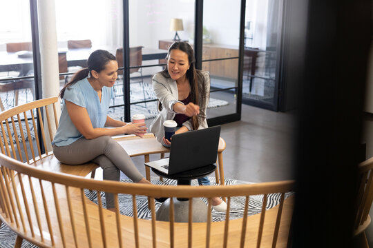 Multiracial creative businesswomen discussing over laptop while sitting in office