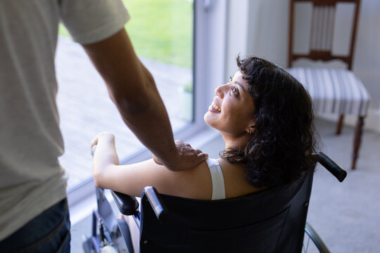 Mid section of a man putting his hand on shoulder of his disabled wife on wheelchair at home