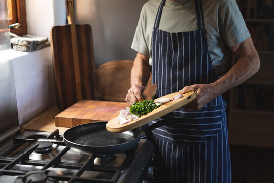 Midsection of caucasian mature man in apron cooking food in kitchen at home